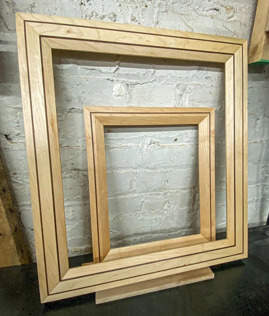Three handcrafted natural wood frames, two with fine walnut inlays, photographed in the workshop